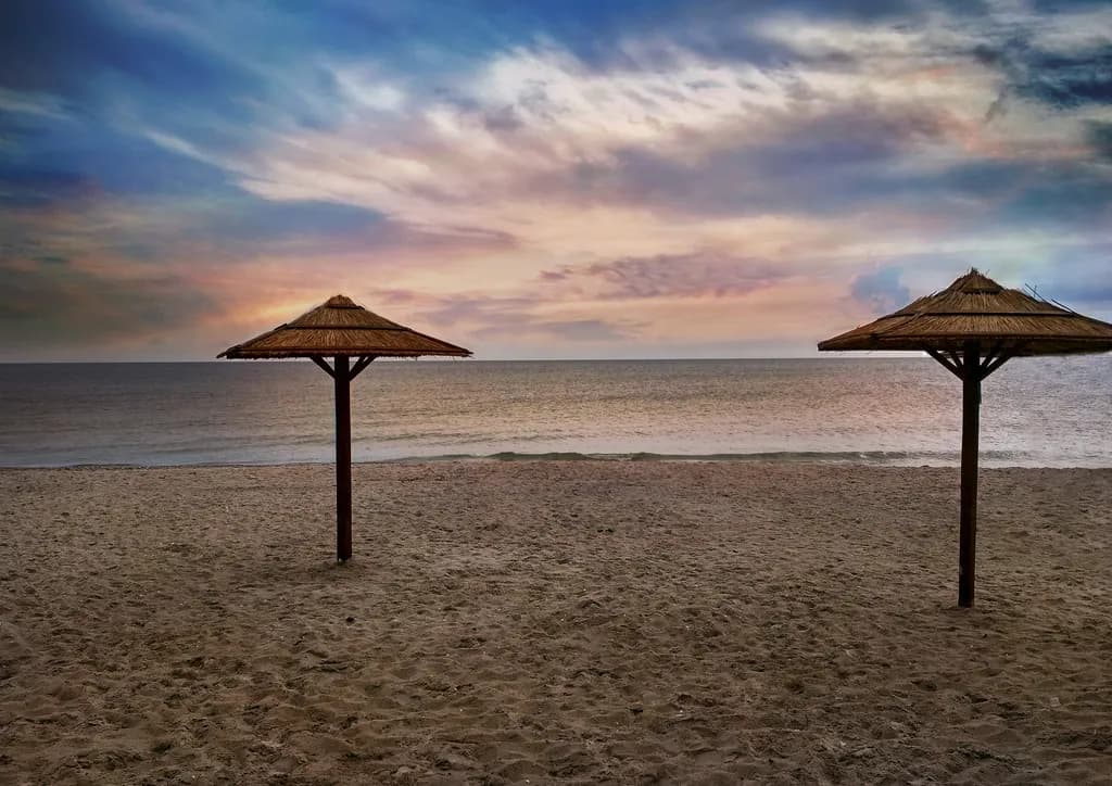 Serenity at Dusk: Tranquil Beachscape with Umbrellas and a Colorful Sky
